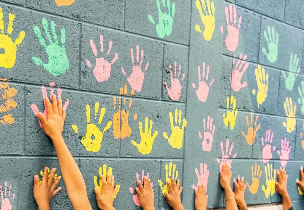 Colourful handprints on a wall with hands reaching up, representing connection, inclusion, and community support